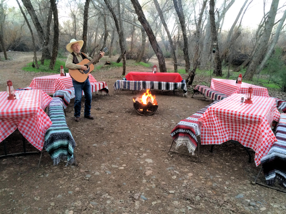Cowboy playing guitar and singing around some picnic tables